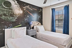 A bedroom with two beds, a nightstand, a Star Wars-themed wall mural, and a window with curtains. - Windsor at Westside - 25962 (Kissimmee)