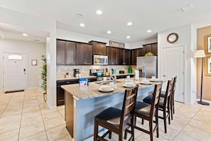 A modern kitchen with dark wood cabinets, a granite countertop, and a central island with bar stools. - Windsor at Westside - 25962 (Kissimmee)
