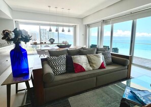 Un saló modern amb un sofà, una taula de menjador i una finestra gran que dona a l'oceà.