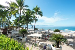 A beachside resort with palm trees, sun loungers, and umbrellas. - Luxury Oceanfront Corner Condo | Icon Vallarta (Puerto Vallarta)