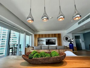 A modern living room with a large flat-screen TV, a wooden accent wall, and a dining area with a large table and chairs. - Luxury Oceanfront Corner Condo | Icon Vallarta (Puerto Vallarta)