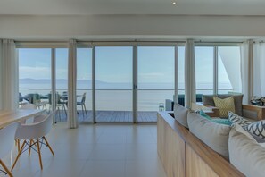 Un interior modern amb zona de dinar, seients per a sofà i vista al mar a través de grans portes de vidre.