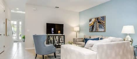 A living room with a sofa, armchair, TV, and artwork on the wall.