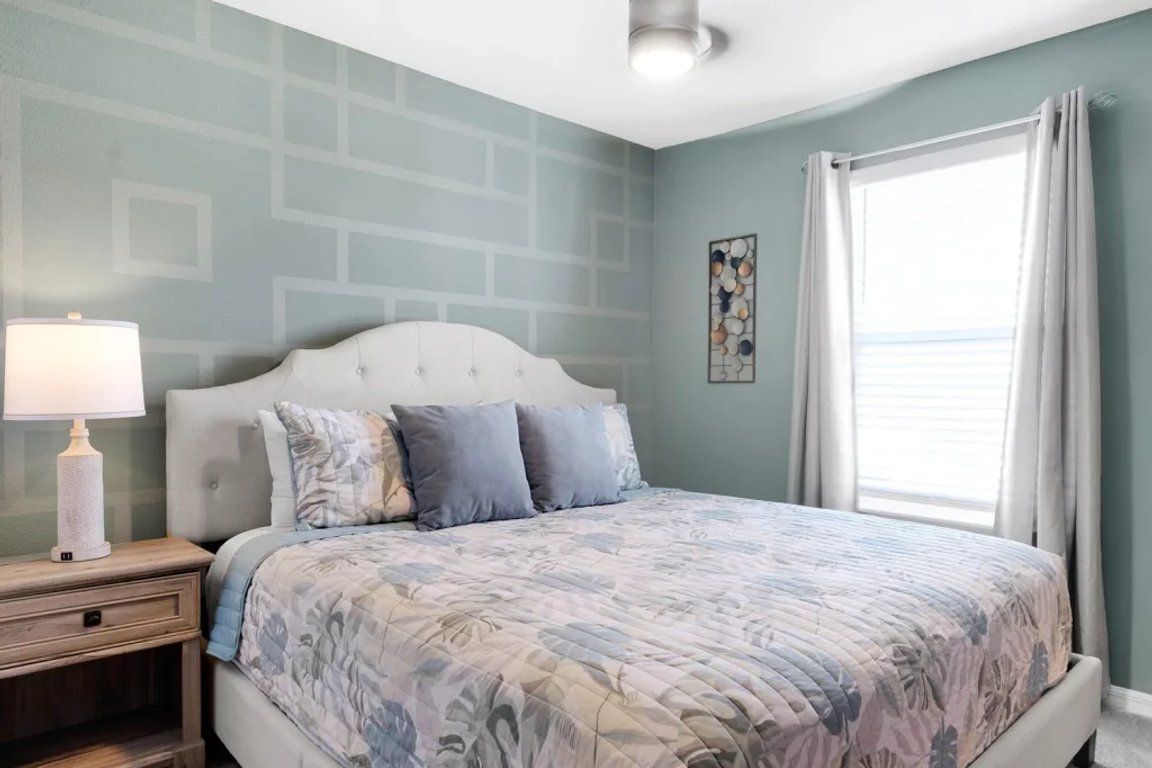 A bedroom with a bed, nightstand, lamp, and a window with curtains.