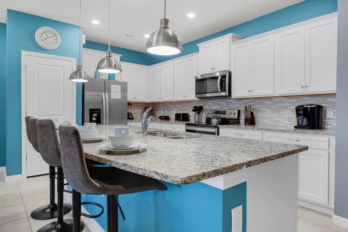 A modern kitchen with white cabinets, a granite countertop, stainless steel appliances, and bar stools.