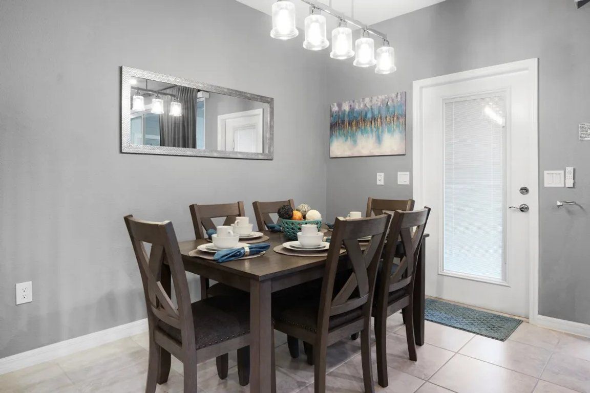 A dining area with a table set for four, chairs, a mirror, and a door with a window.
