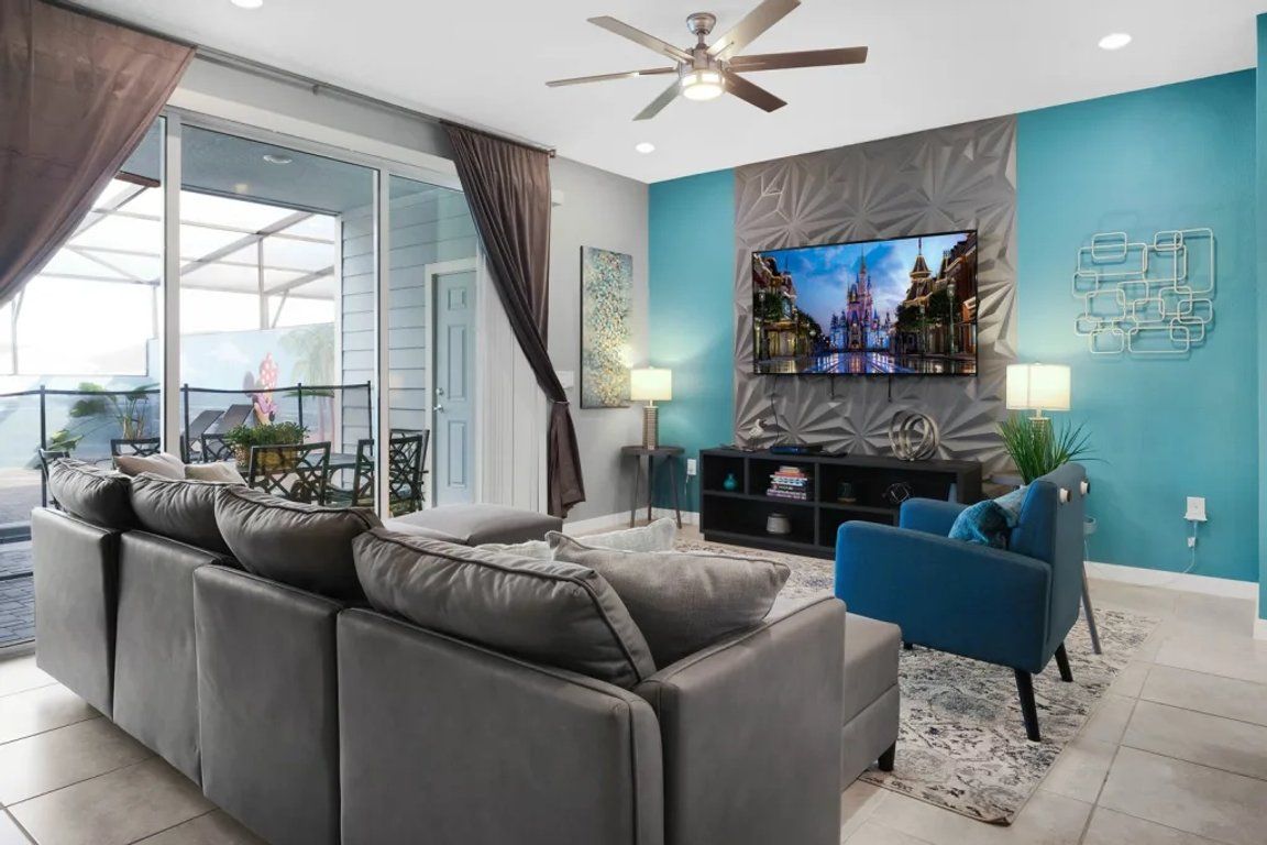 A modern living room with a sofa, a blue armchair, a flat-screen TV, and a ceiling fan.