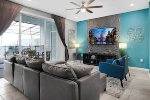 Un salon moderne avec un canapé, un fauteuil bleu, un téléviseur à écran plat et un ventilateur de plafond.