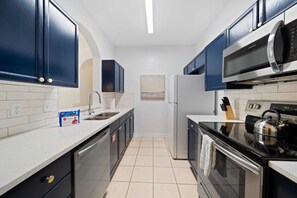 Eine moderne Küche mit dunkelblauen Schränken, Edelstahlgeräten und einem Fliesenboden.