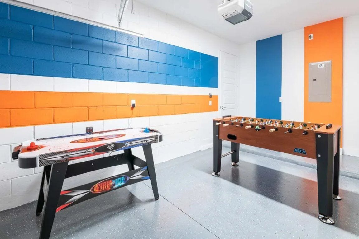 A room with two foosball tables, one with a red and black table and another with a wooden table.
