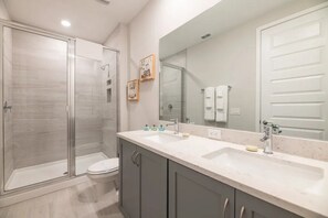 Un baño moderno con ducha envuelta en vidrio, inodoro, lavamanos con espejo y armarios.