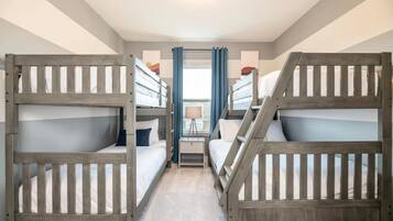 Une chambre avec des lits superposés, une table de chevet, une lampe et une fenêtre avec des rideaux.