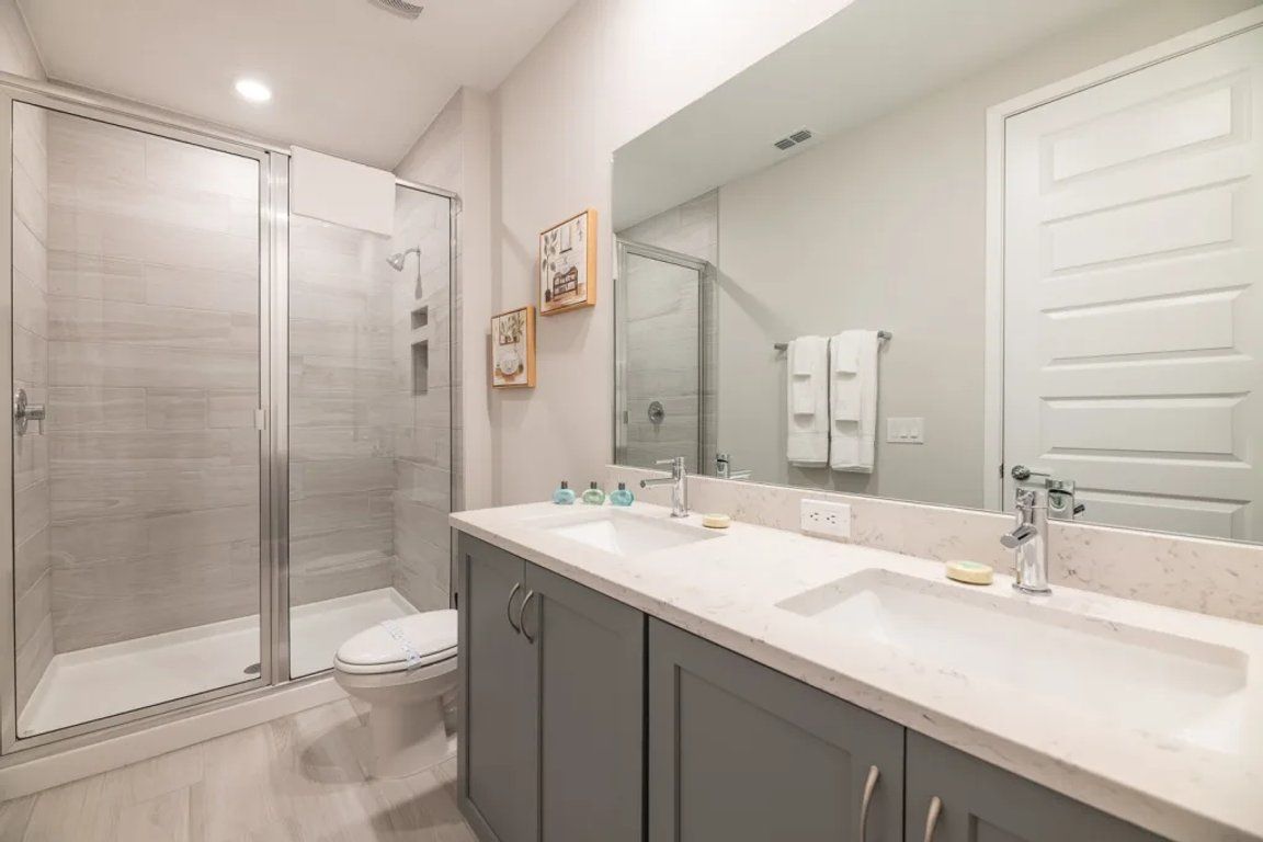 Un bagno moderno con doccia in vetro, un water, un lavandino con specchio e mobiletti.