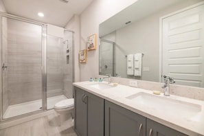 Un bagno moderno con doccia in vetro, un water, un lavandino con specchio e mobiletti.
