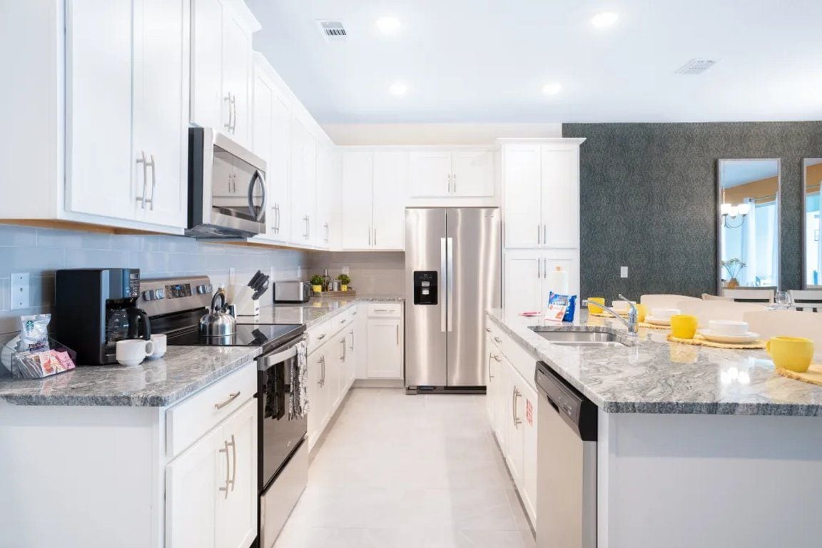 A modern kitchen with white cabinets, stainless steel appliances, and a marble countertop.