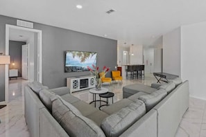 A modern living room with a grey sofa, a flat-screen TV, and a dining area with yellow chairs. - Vista Cay - 28983 (Orlando)