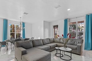 A modern living room with a sectional sofa, a dining table with chairs, and a chandelier. - Vista Cay - 28983 (Orlando)