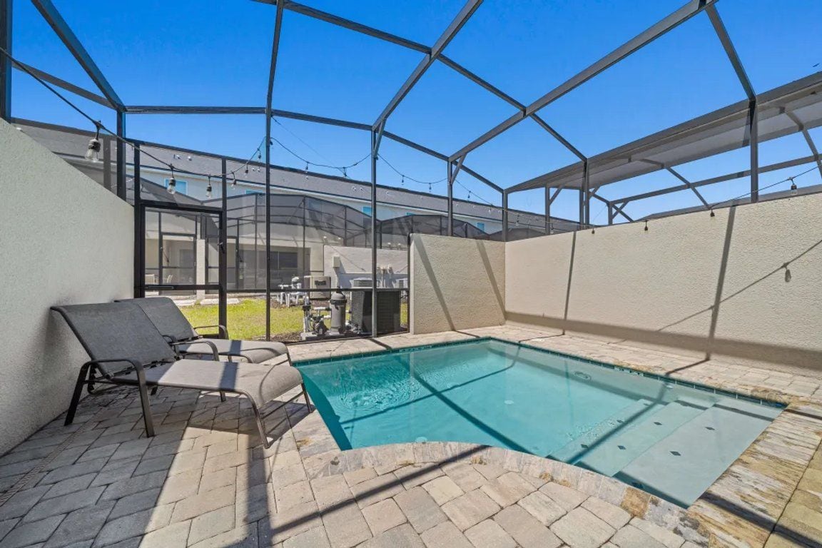 An indoor swimming pool with a glass ceiling, a lounge area with chairs, and a view of the outside.