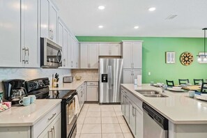 A modern kitchen with white cabinets, stainless steel appliances, and a green accent wall. - Solara Resort - 29105 (Kissimmee)