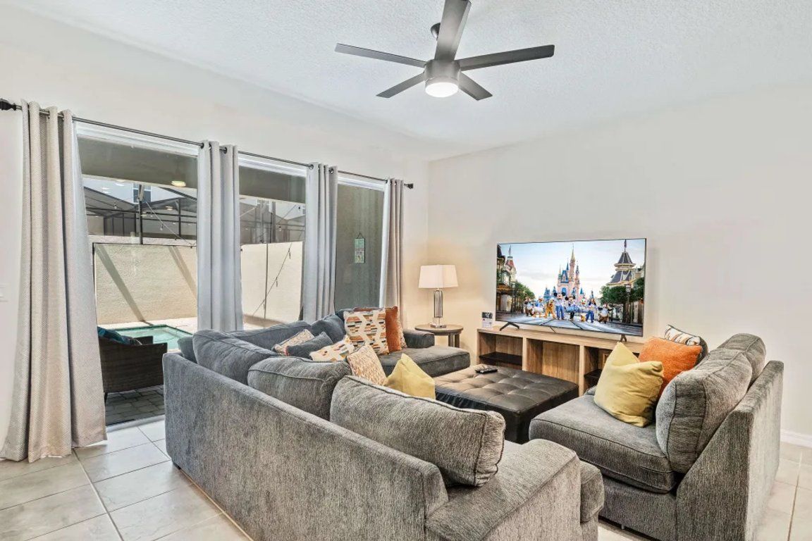 A living room with a grey sofa set, a flat-screen TV, and a ceiling fan.