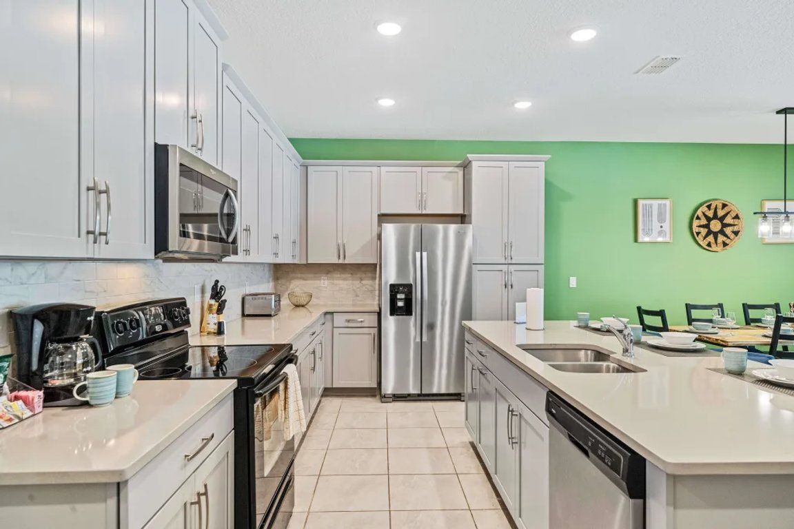 A modern kitchen with white cabinets, stainless steel appliances, and a green accent wall.