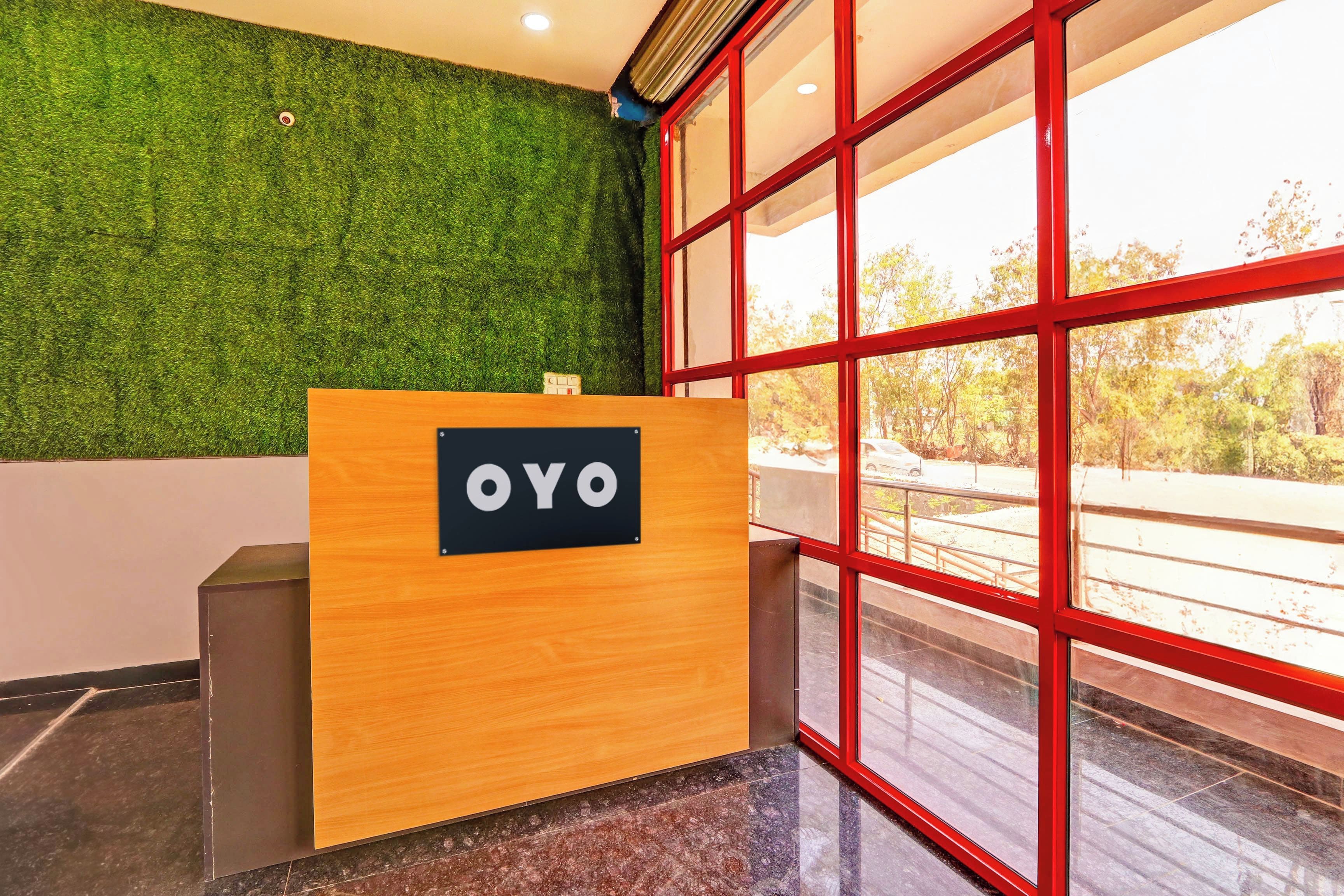 Un mostrador de recepción con un cartel que dice 'OYO' en un vestíbulo moderno con una pared verde y ventanas grandes.