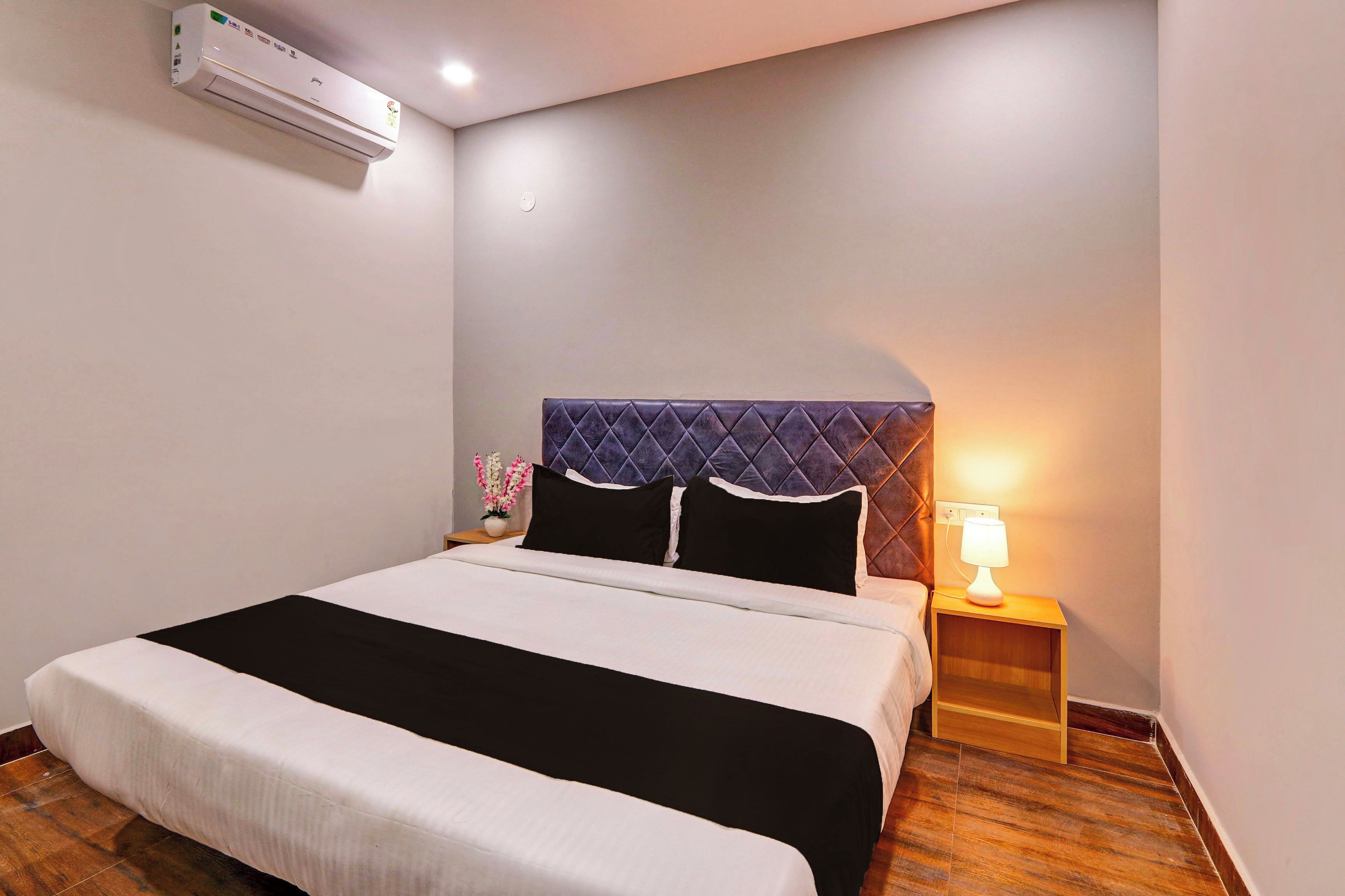 Habitación de hotel con cama, mesita de noche con lámpara, equipo de aire acondicionado y un enchufe de pared.