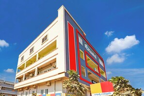 Un edificio de varios pisos con fachada plana, balcones y un cielo azul despejado al fondo.