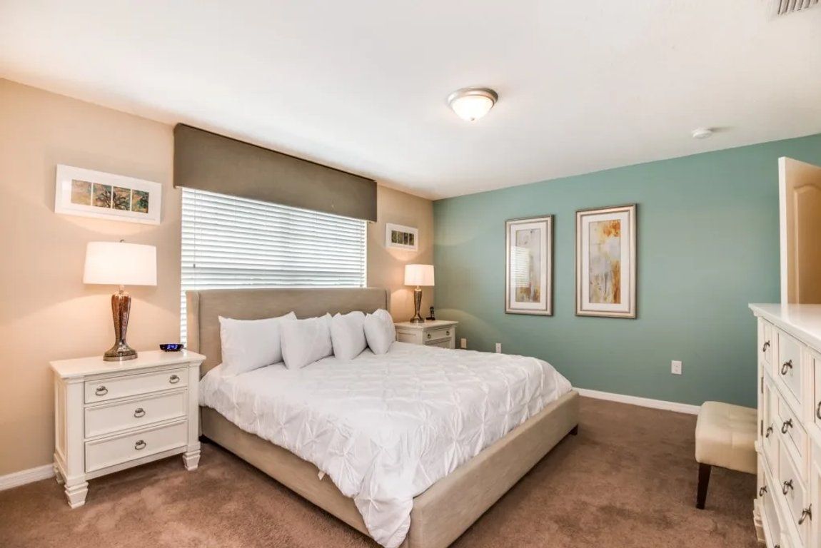 A bedroom with a bed, nightstands, a dresser, and wall art.