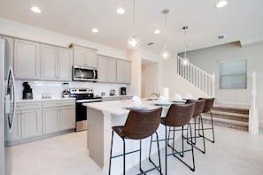 A modern kitchen with white cabinetry, stainless steel appliances, and a central island with bar stools. - Windsor at Westside - 3797 (Kissimmee)