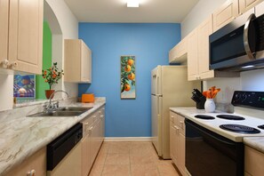 A compact kitchen with a sink, stove, microwave, and refrigerator. - Windsor Palms - 35432 (Kissimmee)
