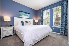 A bedroom with a large bed, two bedside tables, a window with blinds, and a blue wall. - Solara Resort - 30486 (Kissimmee)