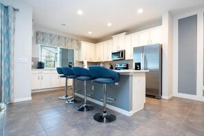 A modern kitchen with white cabinets, a stainless steel refrigerator, and a bar area with blue bar stools. - Solara Resort - 30486 (Kissimmee)