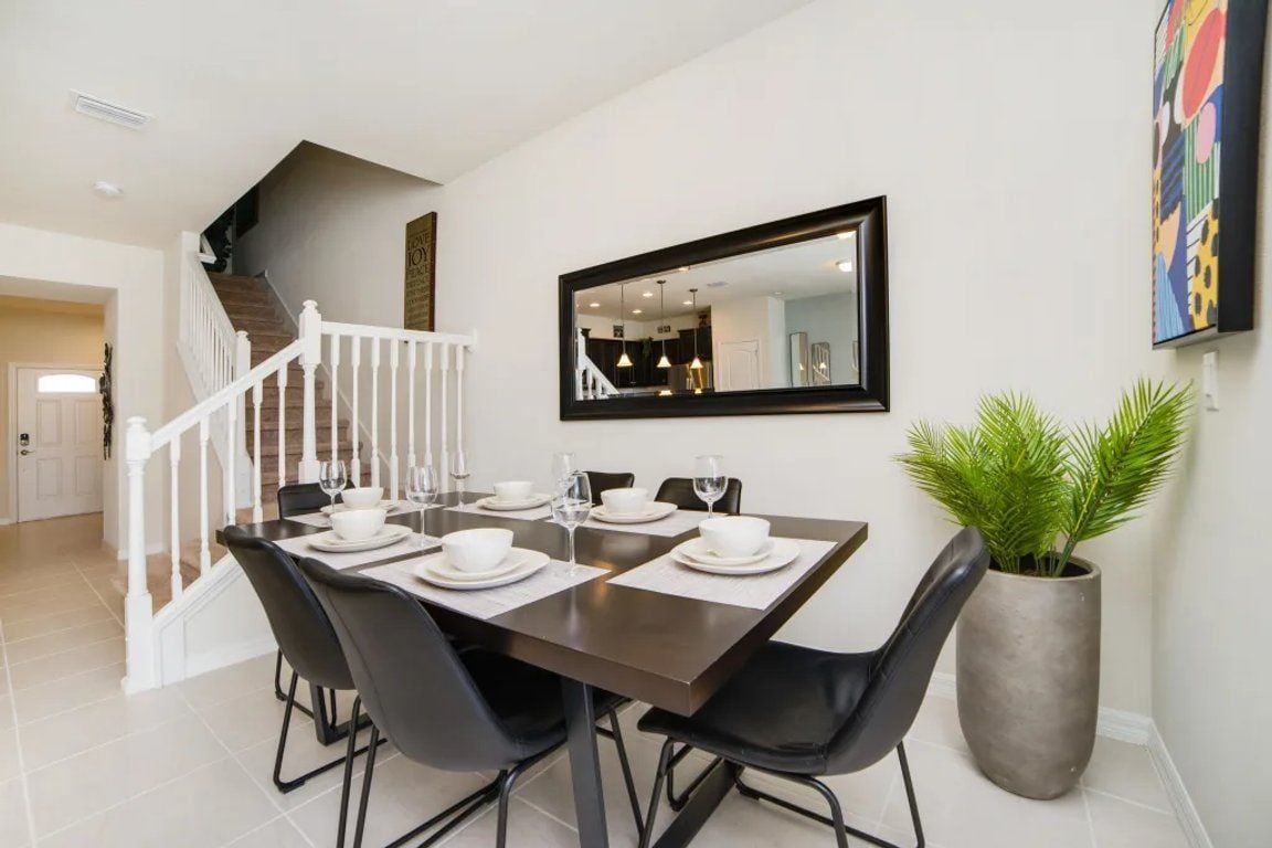 A dining area with a table set for six, a staircase, and a large mirror on the wall.