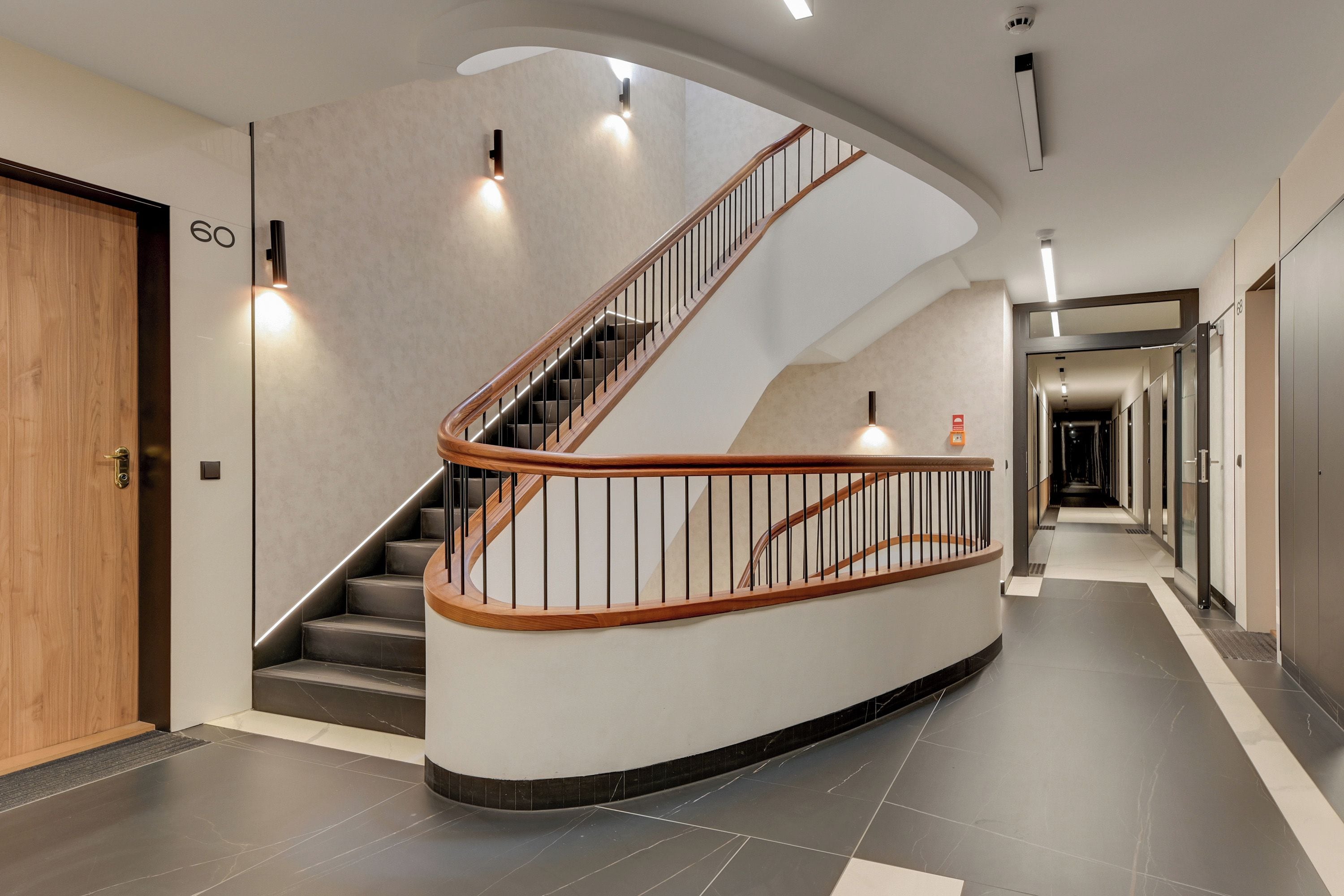 Una escalera curva con barandillas de madera y balaustradas de metal negro, que conduce a un rellano con una puerta marcada con el número '60'.