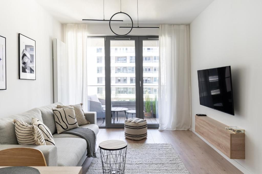 Una sala de estar moderna con un sofá, un televisor y vista al balcón exterior a través de un ventanal.