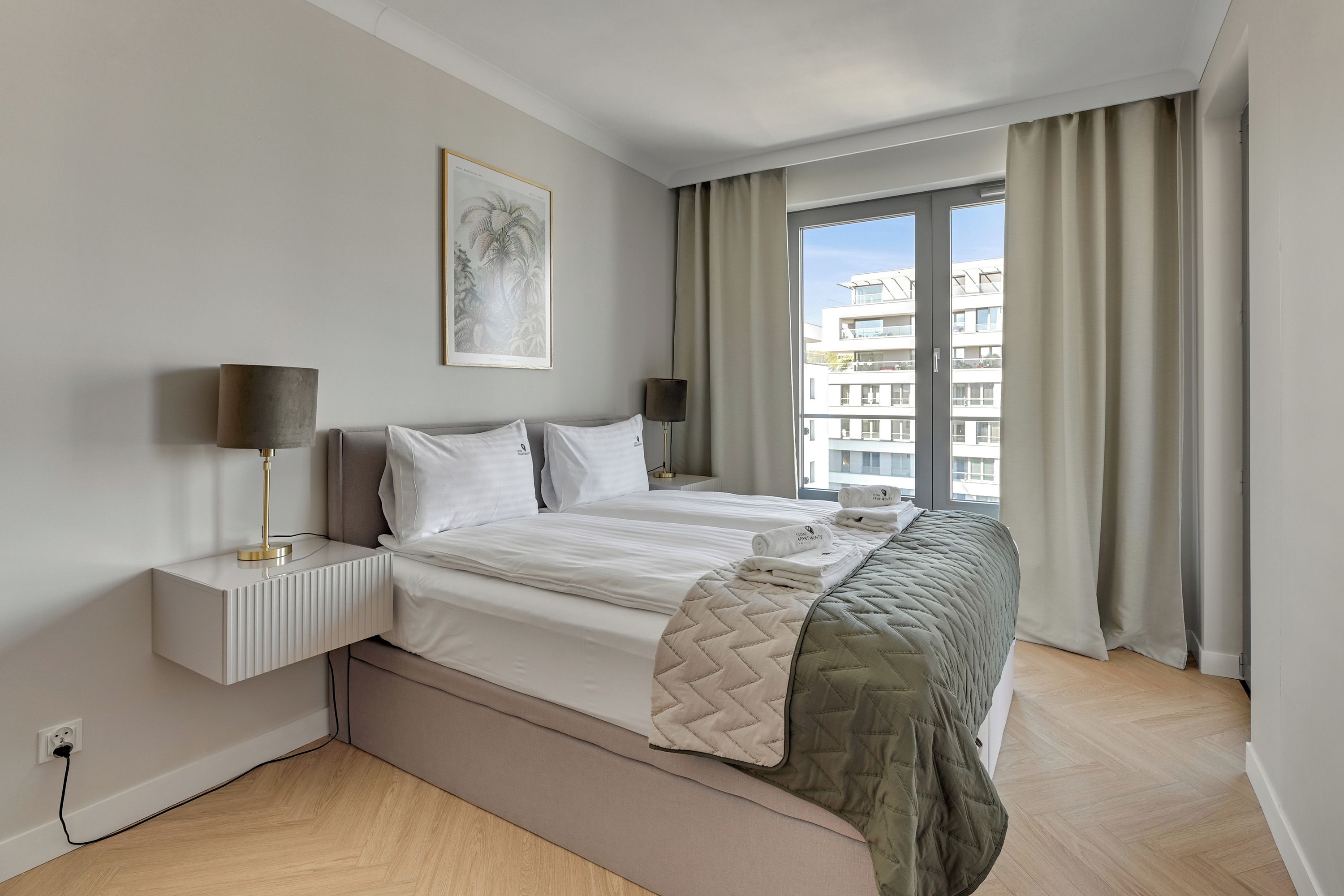A hotel room with a bed, bedside tables, a lamp, a window with curtains, and a wall-mounted picture.