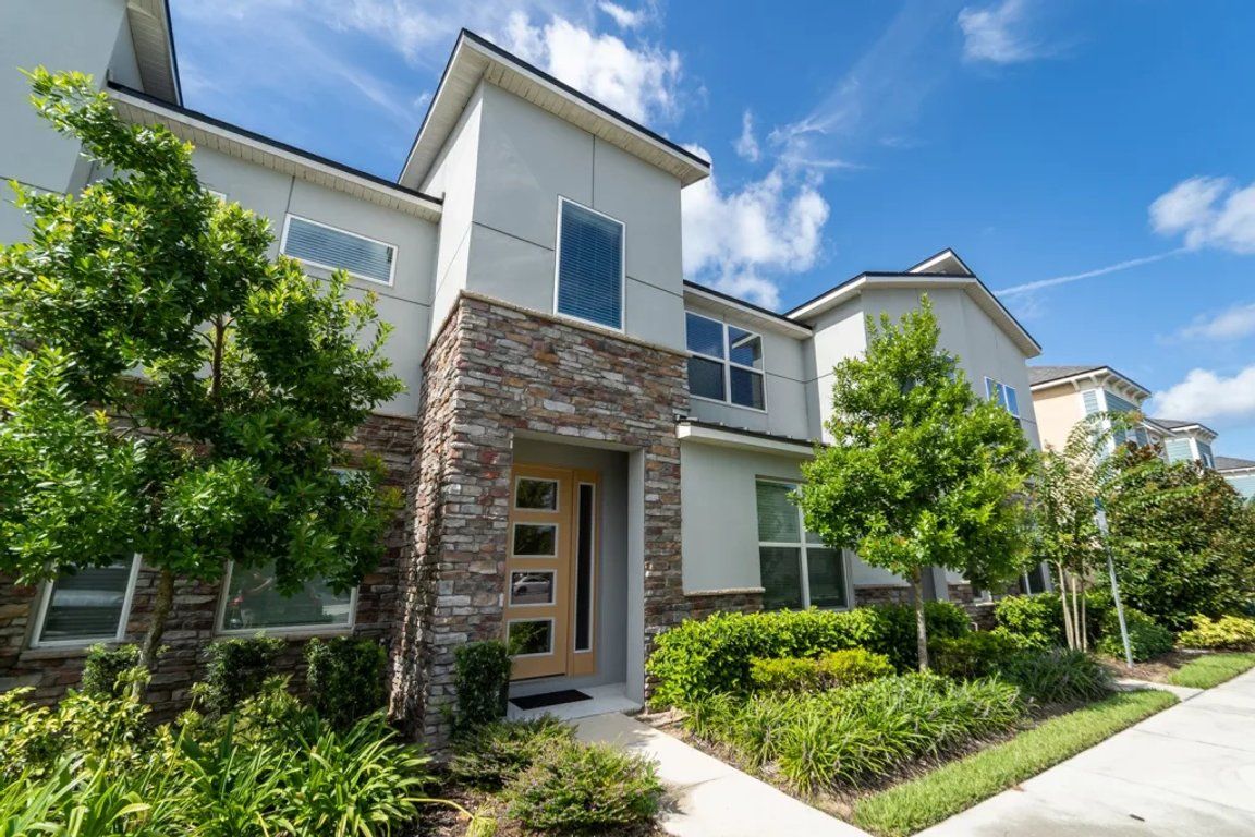A modern two-story residential building with a stone facade, large windows, and a well-maintained garden.
