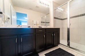 A modern bathroom with a large mirror, dark cabinetry, a shower with a glass door, and a visible hairdryer. - Solara Resort - 6112 (Kissimmee)