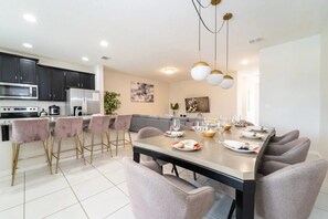 A modern kitchen with dark cabinets, a stainless steel refrigerator, and a dining area with a large table set for six. - Solara Resort - 6112 (Kissimmee)
