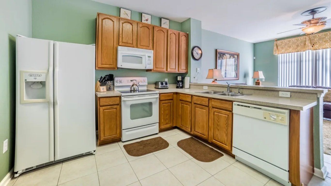 Una cocina con armarios de madera, un refrigerador blanco, un microondas, una estufa, un lavaplatos y un lavamanos.