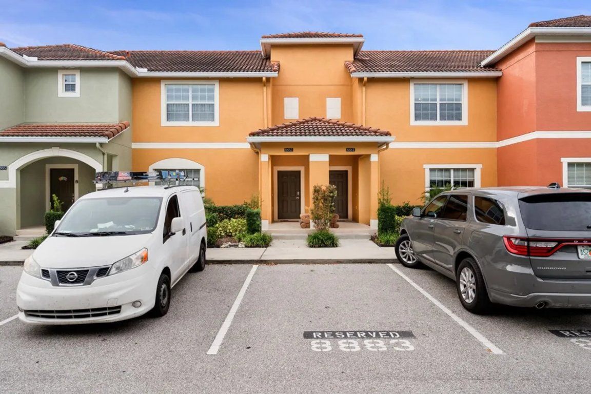 A parking lot with two cars, one white and one gray, parked in front of a building with a red-tiled roof.