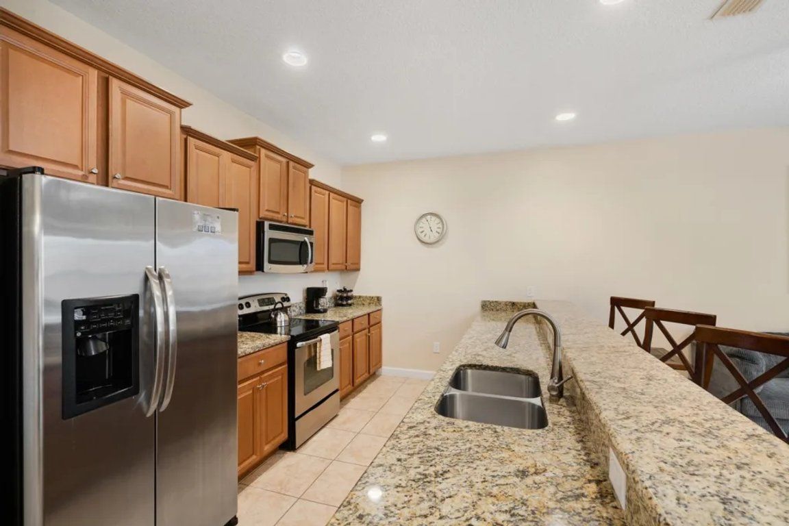 A kitchen with a stainless steel refrigerator, microwave, oven, granite countertop, and a sink.