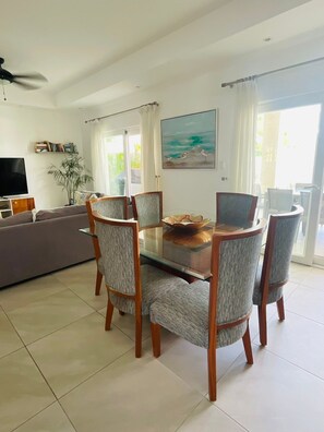 Un coin repas avec une table en verre entourée de chaises, un canapé, un téléviseur et un tableau représentant des oiseaux accroché au mur.