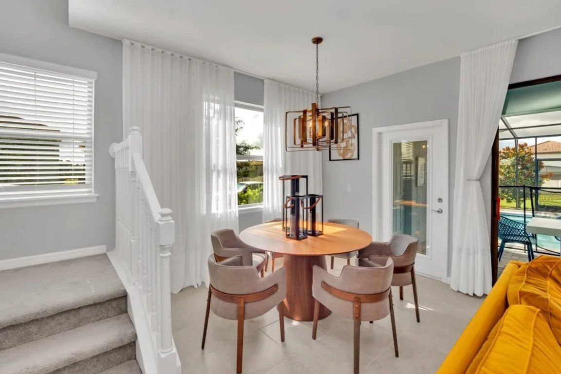 A dining area with a round table and chairs, a chandelier, and a view of a pool through a glass door.