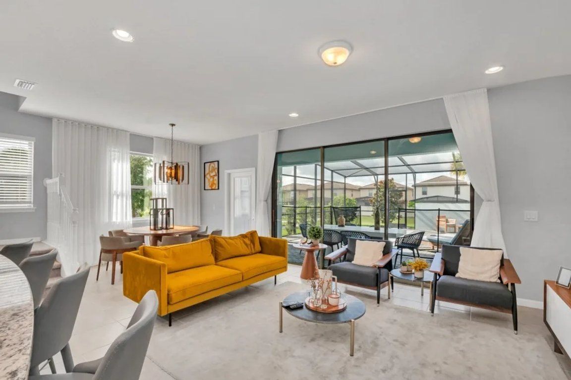 A modern living room with a yellow sofa, grey armchairs, and a coffee table. There is a large window with a view of the outdoors.