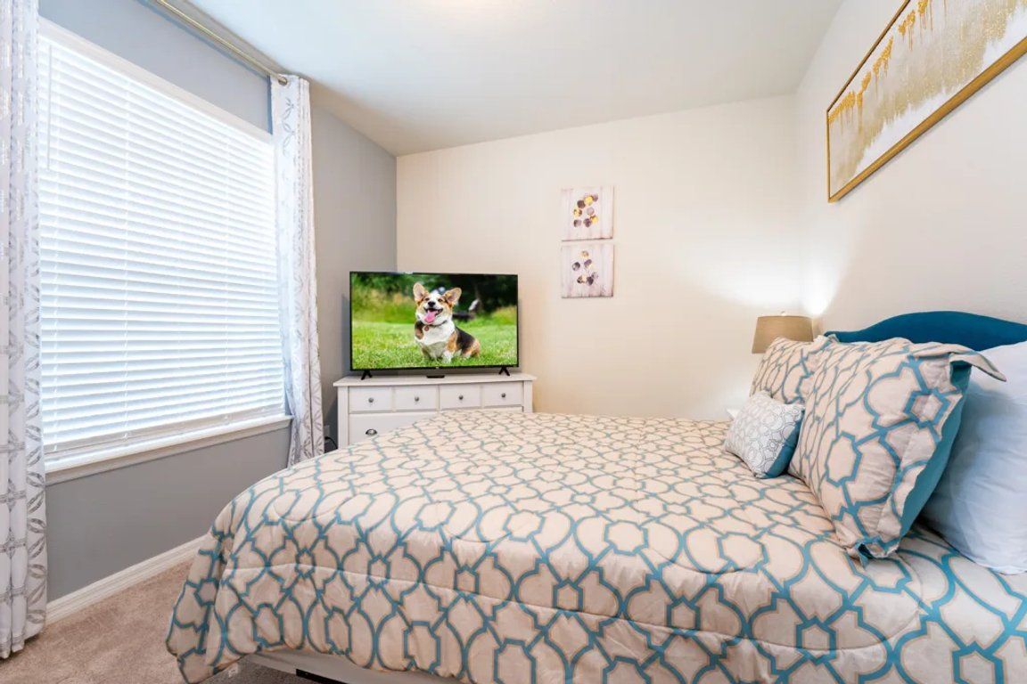 Un dormitorio con cama, televisión, ventana con cortinas y decoración en la pared.