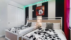 A hotel room with two beds, each with a Mickey Mouse themed bedspread, a white door, a wall with a Mickey Mouse painting, and a red curtain. - Storey Lake - 7330 (Kissimmee)