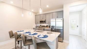Une cuisine moderne dotée d’un îlot central, d’appareils électroménagers en acier inoxydable et de luminaires suspendus.