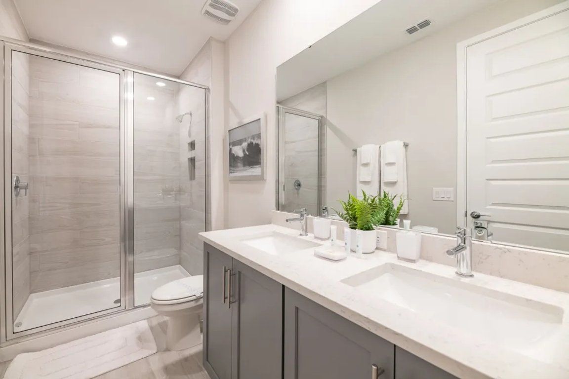 A modern bathroom with a glass-enclosed shower, a large mirror, and a vanity with a sink and countertop.